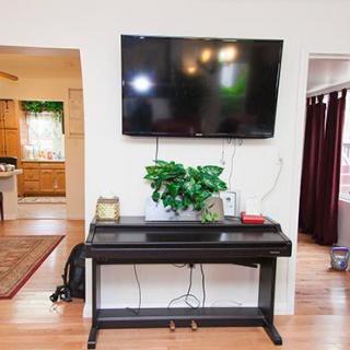 A modern living room with a wall-mounted television above a digital piano, accompanied by a green plant and decorative items.