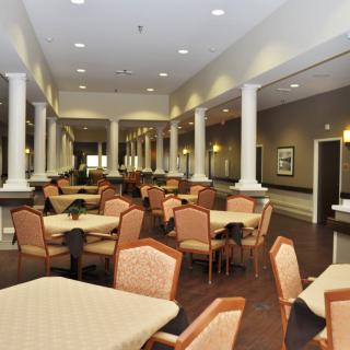 An elegant dining area featuring neatly arranged tables and chairs, illuminated by soft lighting and adorned with classical columns.