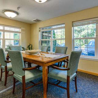 A cozy dining room with a wooden table and chairs, illuminated by natural light through large windows.