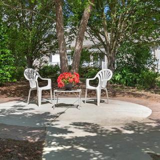 A peaceful garden setting with two white chairs and a table adorned with red flowers, surrounded by lush greenery.