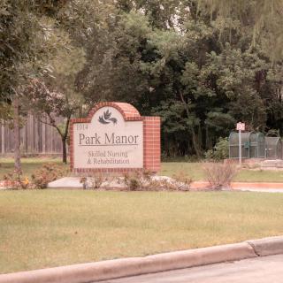 A sign at the entrance of Park Manor, surrounded by greenery and trees.
