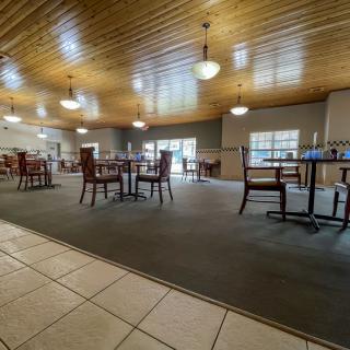 A spacious restaurant dining area with wooden ceilings and a carpeted floor, featuring tables and chairs under ceiling lights.