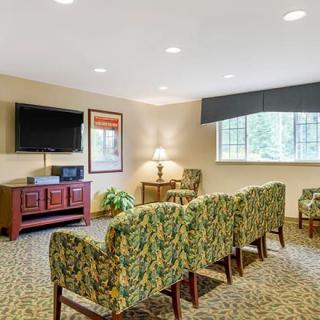 A comfortable waiting room with patterned chairs facing a television, featuring a lamp and artwork on the walls.