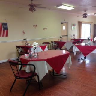 A cozy dining room with red tablecloths and neatly arranged tables, featuring a decor that includes an American flag on the wall.