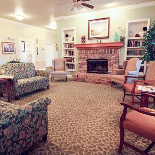 A cozy living room featuring a fireplace, surrounding sofas and chairs, and bookshelves lining the walls.