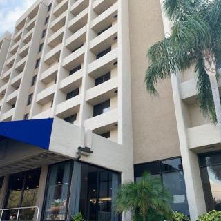 A multi-story hotel building with a blue awning at the entrance and palm trees nearby.