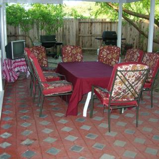 An outdoor patio with a dining set featuring a table covered with a burgundy cloth and chairs with patterned cushions.
