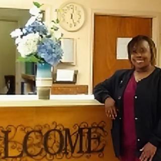 A woman standing next to a welcome desk in a reception area with flowers and a clock.