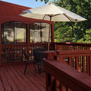 A cozy outdoor patio with a table and chairs under a large umbrella, surrounded by trees.