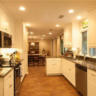 A modern kitchen with white cabinets, stainless steel appliances, and wood flooring.