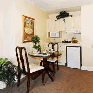A cozy dining area with a small kitchenette, featuring a table and chairs, elegantly decorated with plants and artwork.
