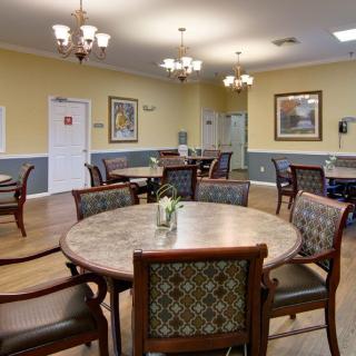 A well-lit dining room with multiple round tables and chairs, featuring elegant decor and warm lighting.