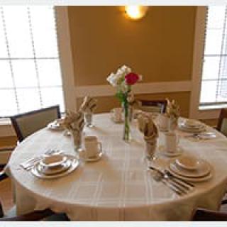 A neatly set dining table with plates, utensils, and a flower vase as the centerpiece.