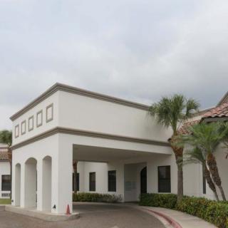 A building with a covered entrance and palm trees under a cloudy sky.