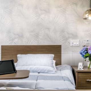 A cozy bedroom with a neatly made bed, a nightstand with flowers, and a modern lamp.