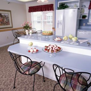 A cozy kitchen with a spacious counter, elegant chairs, and decorative bowls of fruit.