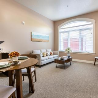 A cozy living room with a sofa, coffee table, and dining area by a large window.