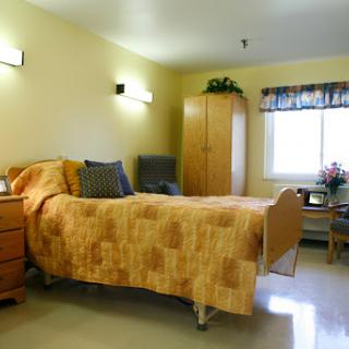 A cozy hospital room featuring a single bed, a wardrobe, and natural light coming through the window.