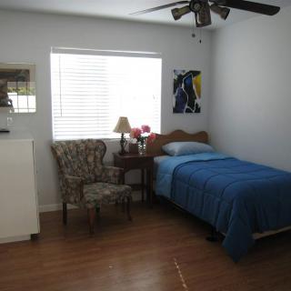 A cozy bedroom with a single bed, blue bedding, and a comfortable chair next to a window.
