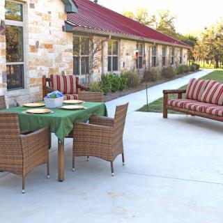 A well-furnished patio area with a table, chairs, and sofa beside a stone building with a red roof.