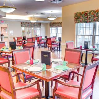 A bright and neatly arranged dining room with red chairs and set tables.