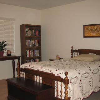 A cozy bedroom with a neatly made bed, bookshelf, and simple decor.