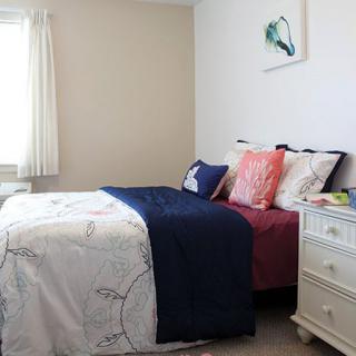 A cozy bedroom with a neatly made bed, featuring colorful pillows and a nightstand by the window.