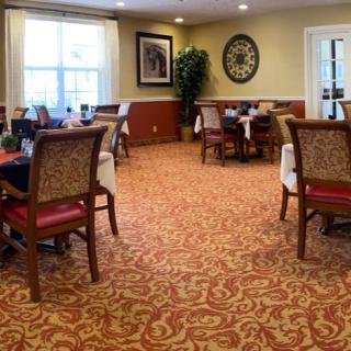 A well-decorated dining room with multiple tables and chairs, featuring elegant carpeting and wall decor.