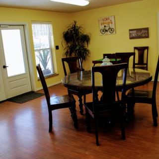 A cozy dining room with a round wooden table and chairs, featuring yellow walls, wall art, and an indoor plant.