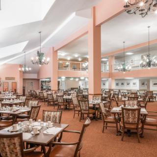 A spacious and elegant dining room with neatly arranged tables and chairs, illuminated by chandeliers.