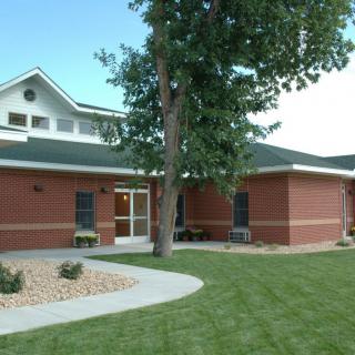 A red brick building with a well-maintained lawn and a tree in front.