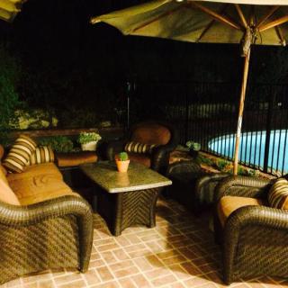 A cozy outdoor patio seating area at night, featuring wicker furniture and an umbrella by the pool.