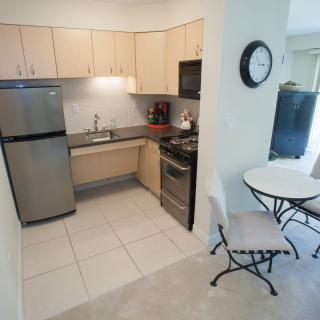 A compact, modern kitchen with light wood cabinets and stainless steel appliances.
