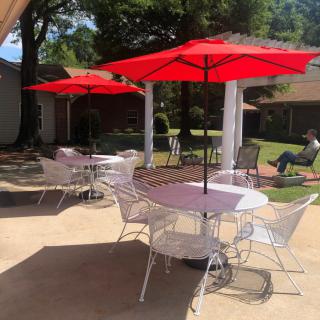 A sunny outdoor patio area with tables, chairs, and red umbrellas.