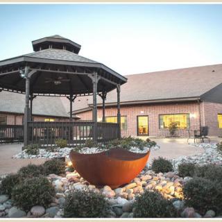 A serene outdoor setting featuring a wooden gazebo surrounded by carefully landscaped gardens and illuminated by soft evening lights.