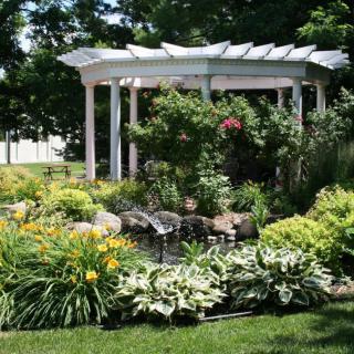 A beautifully landscaped garden featuring a white gazebo surrounded by lush greenery and colorful flowers.