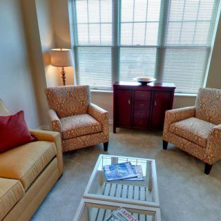 A cozy living room with a sofa, two armchairs, a lamp, and a small cabinet by the window.