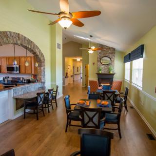 A cozy open-plan dining and living area with a kitchen, featuring wood flooring and a ceiling fan.