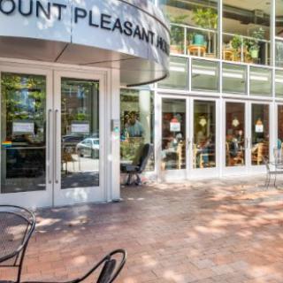 The entrance to a modern cafe with outdoor seating and large glass windows.