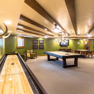 A cozy game room featuring a pool table and shuffleboard under warm lighting.