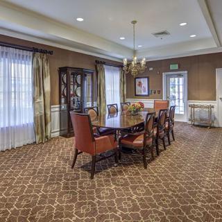 A well-furnished dining room featuring a long table with chairs, elegant chandelier, ornate carpet, and decorative cabinet.