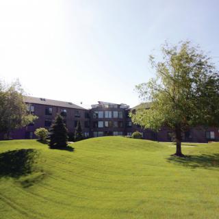 A scenic view of a building with a well-maintained lawn and trees under a clear sky.
