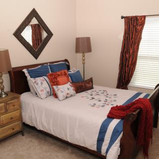 A cozy bedroom with a neatly made bed, decorative pillows, and warm lighting.
