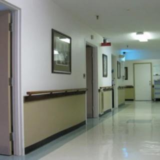 A clean and well-lit hospital hallway with several doors and framed pictures on the walls.
