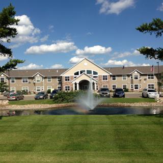 A picturesque residential building with a fountain and lush green lawn under a bright sky.