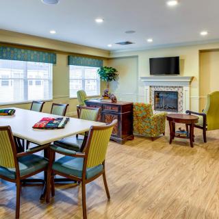 A well-lit meeting room with a conference table, chairs, and a fireplace beneath a television.