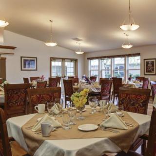 A well-arranged dining room with elegantly set tables and comfortable chairs, featuring warm lighting and large windows.
