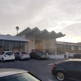 A modern building with a unique roof design, surrounded by parked cars during sunset.