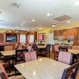 A well-lit dining area featuring multiple tables and chairs, with a kitchen space in the background.