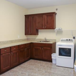 A laundry room with a washing machine, wooden cabinets, and a sink.